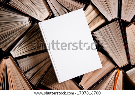 Mockup of closed blank square book rests on open old multicolored books