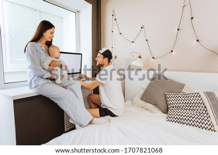 Parents With Baby Working At Home Looking At Computer, Smiling