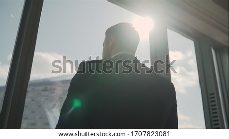 A businessman goes to the window. Side view on Handsome businessman in suit walking outdoor big glass urban airport building. Successful businessman in his office with panoramic windows.