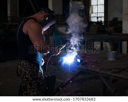 welder works in metal construction - construction and processing of steel components.fitnes and gym in factory. Cutting metal with cutting machine.
welder mask
