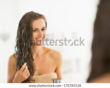 Happy young woman applying hair mask in bathroom Royalty-Free Stock Photo #170783528
