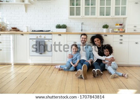 Portrait of happy multiracial young family with little kids sit on warm floor in design modern kitchen, smiling multiethnic parents with small biracial daughters relax in new renovated home together Royalty-Free Stock Photo #1707843814