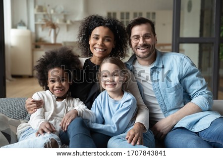 Portrait of happy multiracial young family with little daughters sit on couch look at camera posing, smiling multiethnic parents cuddle hug with small kids girls, enjoy weekend quarantine at home Royalty-Free Stock Photo #1707843841