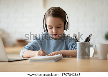 Cute little girl in headphones watch video tutorial drawing in album, small preschooler kid listen to music in earphones painting pictures, child studying online at home, homeschooling concept