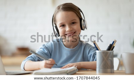 Portrait of smiling little girl wearing wireless headphones drawing at home, happy small preschooler child in earphones have fun painting picture on weekend, studying online on quarantine Royalty-Free Stock Photo #1707844045