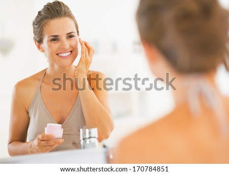 Happy young woman applying cream in bathroom Royalty-Free Stock Photo #170784851