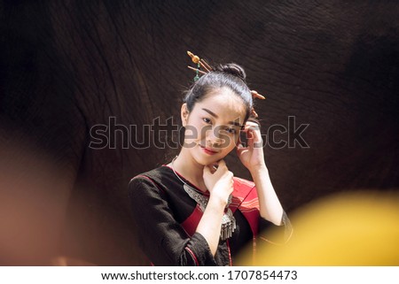 Women wearing native dresses holding a red umbrella and living with elephants. Asian woman and big elephant in the Forest. Elephant with beautiful girl in asian countryside, Surin, Thailand.