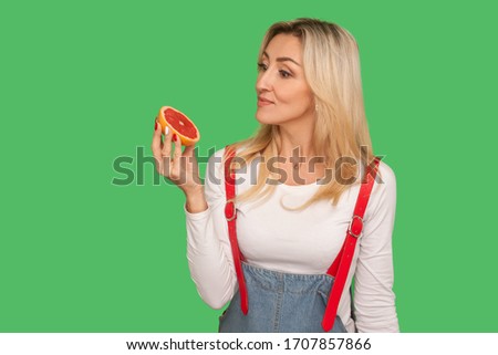 Detoxing food, vitamins for diet. Portrait of pensive adult woman looking at sliced juicy fresh grapefruit with thoughtful expression, healthy nutrition. studio shot isolated on green background
