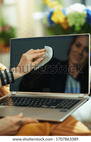Closeup on smiling woman cleaning laptop display with cleaning cloth at home in sunny day.