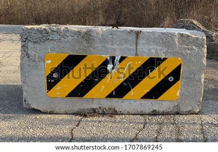 Black and yellow warning sign on a concrete block prohibiting access to a park during covid-19 lockdown to ensure safe social distancing.
