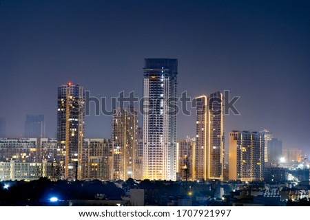 High rise multi story skyscrapers lit up at night with small houses in the foreground at night in gurgaon delhi. Shows the rapid pace of development of the real estate sector with property, offices Royalty-Free Stock Photo #1707921997