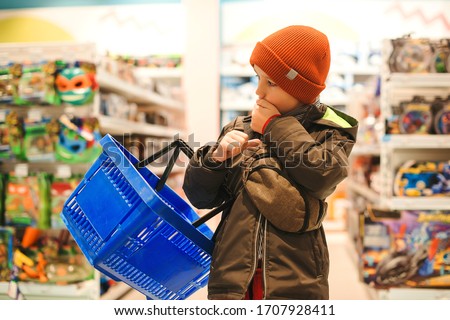 Little boy choosing toy in supermarket. Kid difficult to choose the best toy. Child with shopping basket at the toys shop. Christmas sales. Shopping and sales.