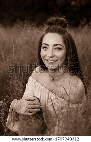A gorgeous young woman sits in a meadow of long grass near Liverpool one summers evening pulling her knee gently towards her chest.