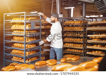 A baker carries a rack of bread at the bakery. Industrial bread production Royalty-Free Stock Photo #1707944335
