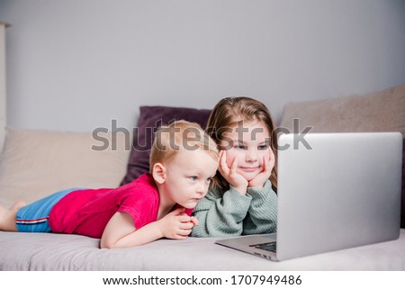 Two children a boy and a girl lie on a sofa in home clothes and watch videos on a laptop