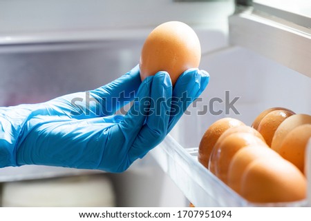 Housewife Wearing Blue Latex Gloves Stocking Fresh Chicken Eggs in Refrigerator. People Panic and Prepare to Pandemic Quarantine. Stay at Home Policy from Government During Coronavirus or COVID-19