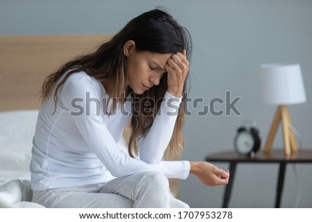 Unhappy woman sitting on bed, feeling depressed, thinking about problems, bad relationship or break up, upset girl touching forehead, feeling lonely, suffering from psychological troubles Royalty-Free Stock Photo #1707953278
