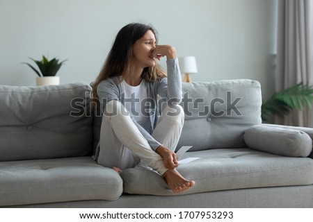 Depressed young woman suffering from break up with boyfriend or divorce with husband, holding torn photo, bad relationship, stressed upset girl crying, feeling lonely, sitting on couch at home alone