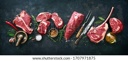 Variety of raw beef meat steaks for grilling with seasoning and utensils on dark rustic board Royalty-Free Stock Photo #1707971875