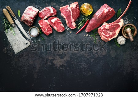Variety of raw beef meat steaks for grilling with seasoning and utensils on dark rustic board Royalty-Free Stock Photo #1707971923