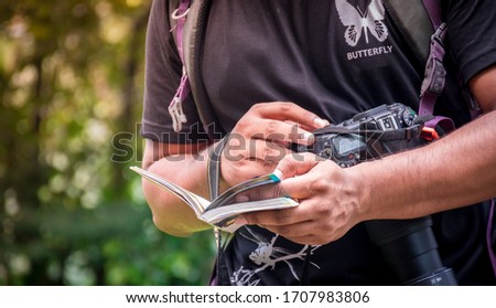 A man reading a guide book while hanging the camera one hand, half body photo Royalty-Free Stock Photo #1707983806