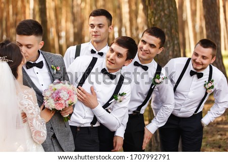 Bride and groom kisses near friends, groomsmen with bow ties and suspender looks at newlyweds at wedding day Royalty-Free Stock Photo #1707992791