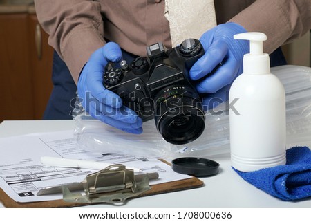 Parcel delivery during self-isolation. A man in rubber gloves takes a camera out of a bubble pack. Nearby lies the form for the delivery of the parcel and there is a spray bottle with disinfectant.