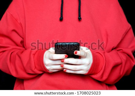 Young girl wearing in red hoodie looks to the screen of black smartphone photo on black background front close up