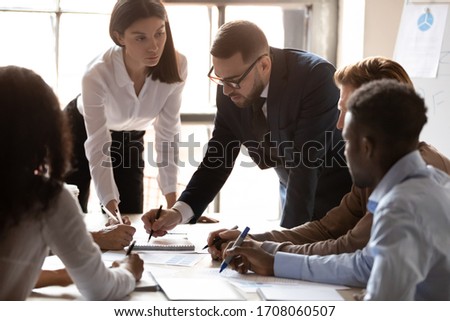 Serious diverse businesspeople sit at office desk brainstorm consider paperwork statistics at briefing, male boss explain business project to multicultural colleagues at meeting, cooperation concept Royalty-Free Stock Photo #1708060507