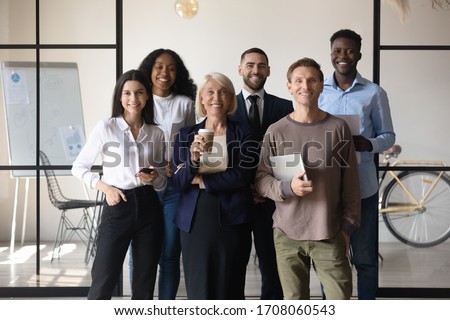 Group portrait of multicultural diverse businesspeople stand together look at camera posing in modern office show unity and support, smiling multiracial colleagues make team picture at workplace