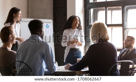Smiling multicultural diverse colleagues brainstorm discuss financial ideas at meeting in boardroom, happy multiethnic coworkers employees talk consider flip chart presentation at briefing together Royalty-Free Stock Photo #1708062667