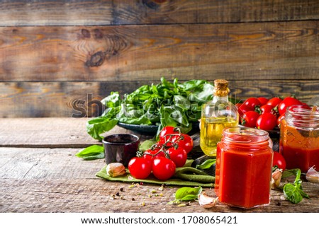 Homemade tomato sauce with basil, garlic and fresh tomatoes. Ketchup, marinara sauce in small jars. On a wooden background, with fresh vegetables and basil.