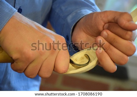 Wooden workshop. Hands carving spoon from wood, working with chisel close up. Process of making wooden spoon. Stock Photo