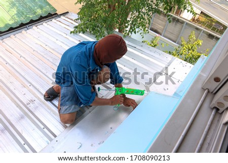 The roof repairman is firing silicone to fix the roof leaks. The photo is used for the advertisement of the house construction business.