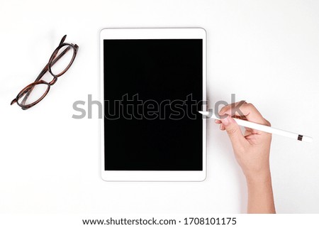 Top view image of woman holding a digital pen writing on a blank screen tablet computer against white background.