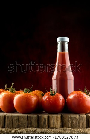 Concept picture of ketchup, with many fresh tomatoes decorated around, placed on a wooden table with the concept of freshness coming out from the sauce bottle on dark background.