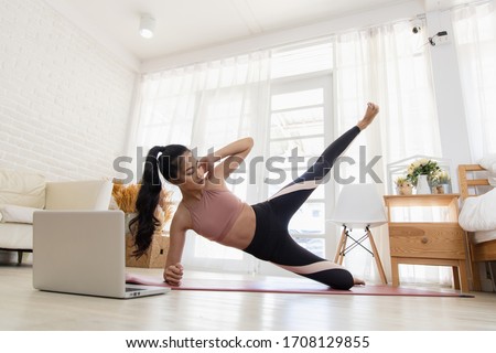 A beautiful Asian woman's fitness at home instead of going to the gym. Her learning new exercises watching online workout tutorials over her computer laptop at home. Exercise concept for good shape Royalty-Free Stock Photo #1708129855