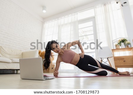 A beautiful Asian woman's fitness at home instead of going to the gym. Her learning new exercises watching online workout tutorials over her computer laptop at home. Exercise concept for good shape Royalty-Free Stock Photo #1708129873