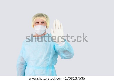 Doctor hand makes a stop sign. White protective gloves. Medical mask on the face. Surgeon in working uniform. No to viruses and diseases. A gesture requiring stopping. Epidemic Landing Page.