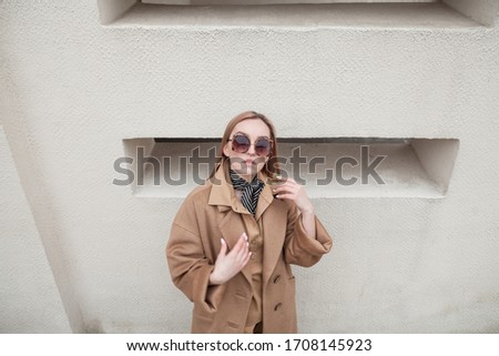 Young pretty beautiful stylish woman in beige woolen coat  standing and posing at white wall background. Fashionable stylish autumn look in pastel colors. Urban fashion, high angle view, soft tones
