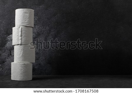 Toilet paper rolls stack besides dark concrete background. White toilet paper with copy space.