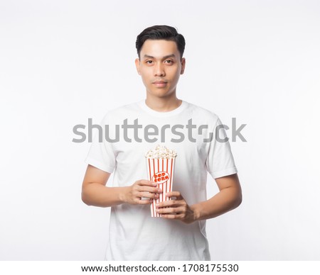 Young asian man in white t-shirt holding popcorn and looking to camera isolated on white background.