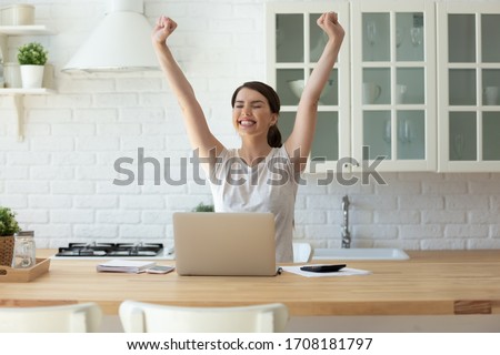 Young attractive woman exulting using calculator and laptop for calculating finance rates looking at screen. Successful girl happy hands up accounting with check credit analytic for mortgage payment. Royalty-Free Stock Photo #1708181797