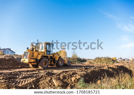 large yellow wheel loader aligns a piece of land for a new building. Preparation of the land for the auction. Leveling the landscape and adding sand for construction. Banner wallpaper. Royalty-Free Stock Photo #1708185721
