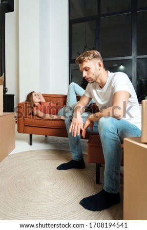 Real estate concept. Vertical photo of young adult family together move in new apartment. Exhausted couple resting in living room, sitting near cardboard boxes