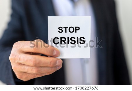 Inscription on sticker - STOP Crisis holding by a man's hand in suit. Unfocused background