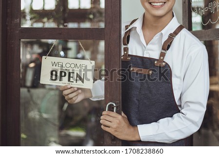 Store owner turning open sign broad through the door glass and ready to service.