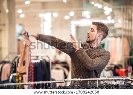 A young man looking for a present for his girlfriend in a department store, taking a picture of some shorts to ask for an advice