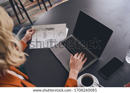 Cropped photo of a blonde female interior designer holding a house plan in her hand