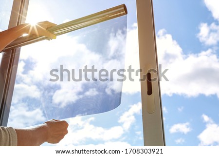 tinted glass in the house. window dimming by dark film. hands apply tint film to the window. tint film on sky background. sky view through tinted glass Royalty-Free Stock Photo #1708303921